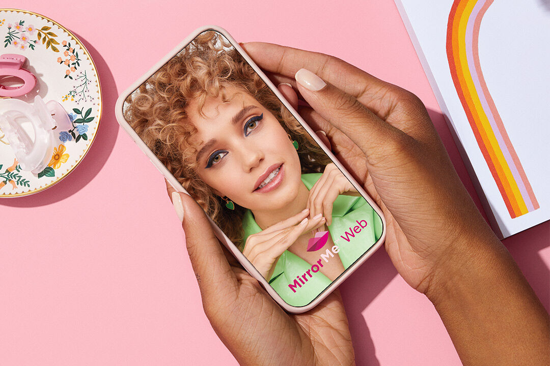 Mano sosteniendo un tel&eacute;fono que muestra la experiencia de prueba virtual MirrorMe de Mary Kay.