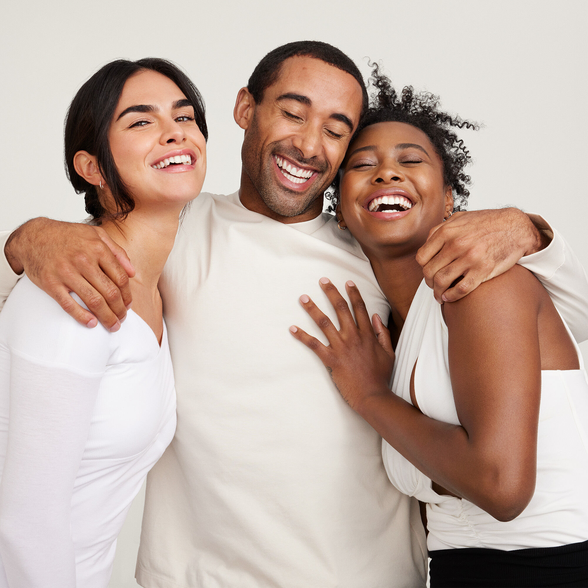 Tres personas juntas, vestidas con tonos claros, frente a un fondo neutro.