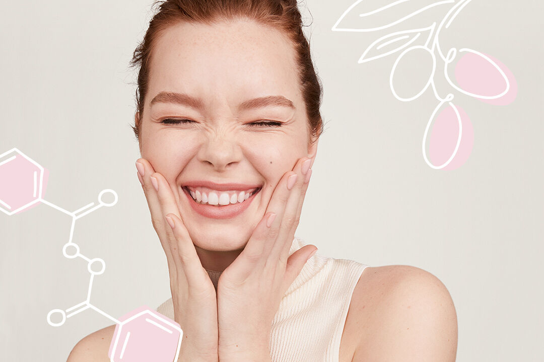 Mujer sonriendo con las manos junto a las mejillas, con ilustraciones de los ingredientes activos de Mary Kay de fondo.