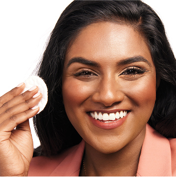 Modelo sonriendo a la c&aacute;mara, prepar&aacute;ndose para retirar el maquillaje de ojos con un algod&oacute;n